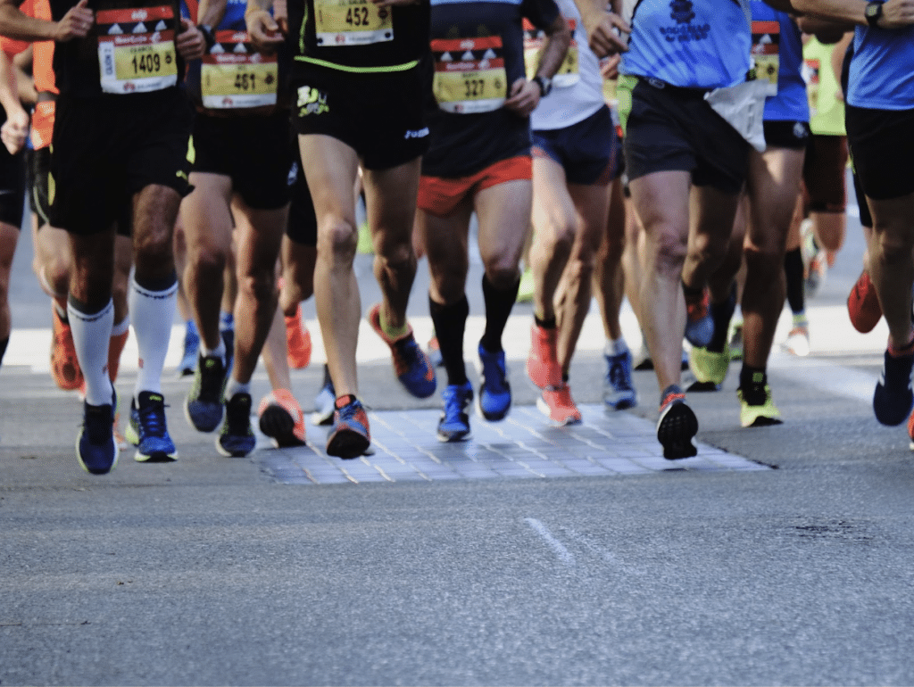 Many running feet are pictured at the starting line of a marathon on a city street.