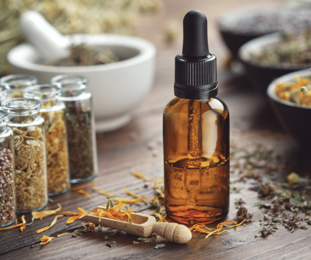 Amber essential oil bottle surrounded by many dried herbs used for homeopathic medicine.