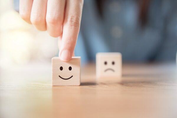 Close up image of a hand choosing between a smiling face icon and a frowning face icon. The hand is pointing to the best choice, happy.
